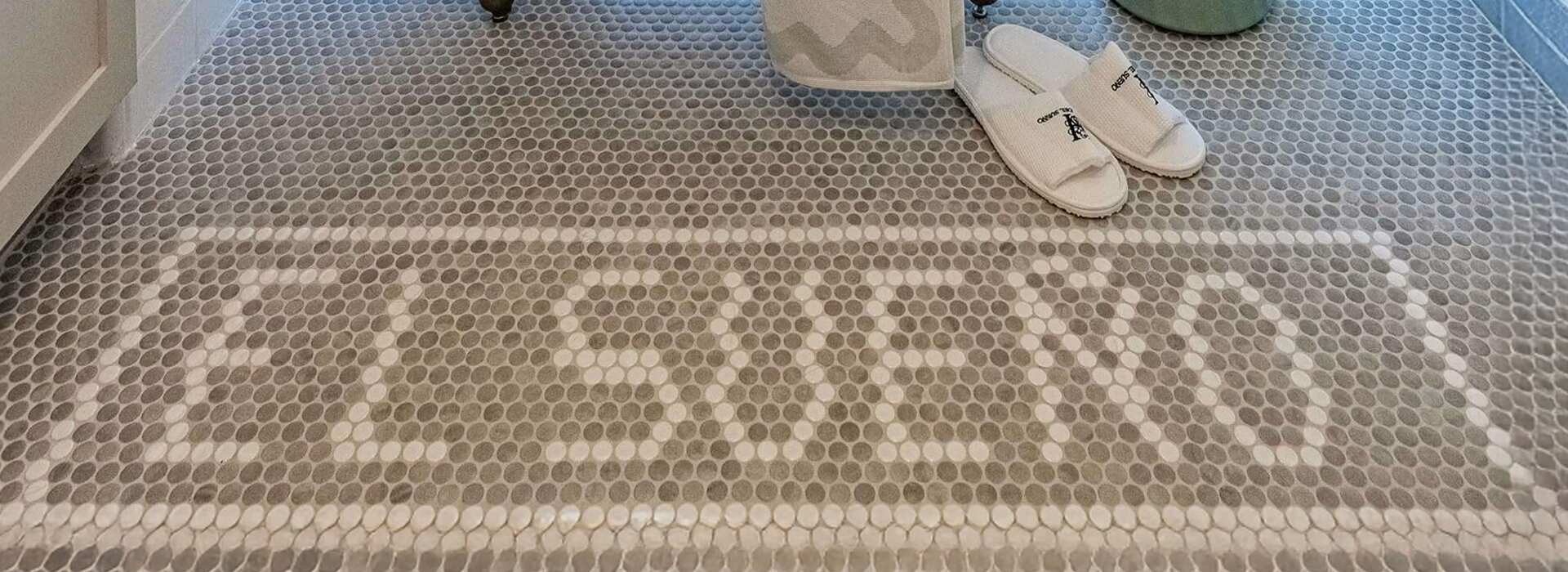 El Sueño spelled in mosaic bathroom tile, with white slippers beside it.